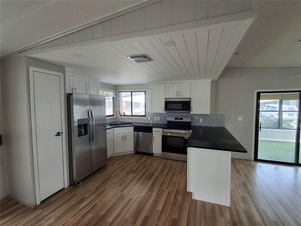 A kitchen features white cabinets, stainless steel appliances, black countertops, and light wood-look flooring — 141 RAROTONGA ROAD, NORTH PORT, FL