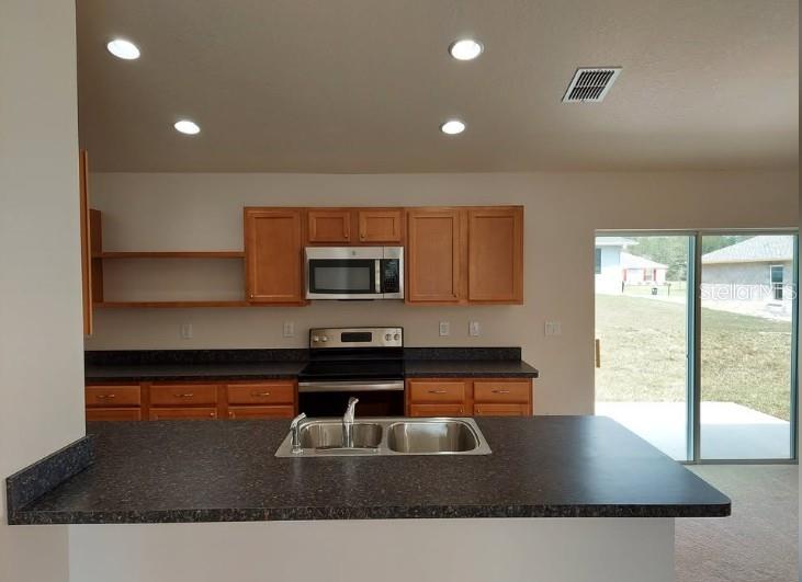 A kitchen features wood cabinets, dark countertops, stainless steel appliances, and a sliding glass door — 15492 SW 34TH COURT ROAD, OCALA, FL