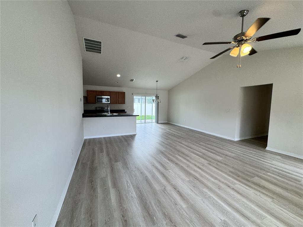 An open-concept living area features light wood-look flooring, vaulted ceilings, and an adjacent kitchen — 15492 SW 34TH COURT ROAD, OCALA, FL