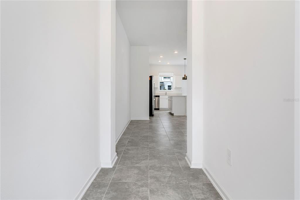 A hallway with gray tile flooring leads into a bright kitchen with white cabinetry — 264 NINE IRON DRIVE, DAVENPORT, FL