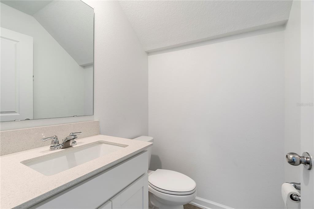 A small bathroom features a white vanity with a quartz countertop, mirror, and toilet — 264 NINE IRON DRIVE, DAVENPORT, FL