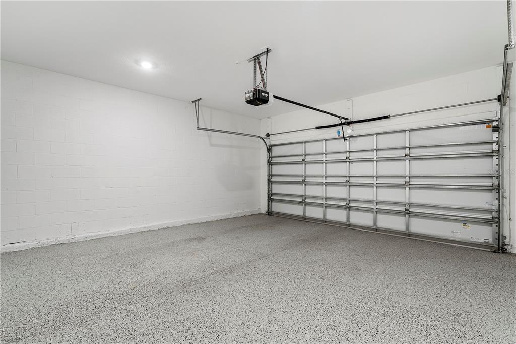 An empty garage features white painted block walls, a speckled epoxy floor, and a door opener — 264 NINE IRON DRIVE, DAVENPORT, FL