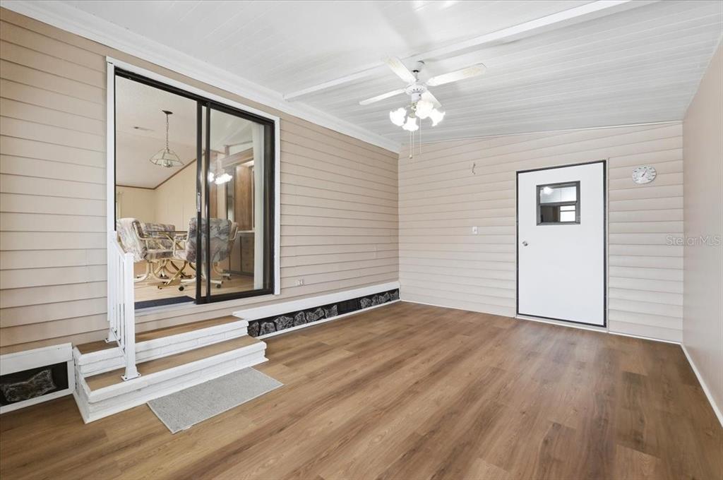 A sunroom features light wood-look flooring, beige horizontal siding, a ceiling fan, and sliding glass doors — 1798 FOX HILL DRIVE, LAKELAND, FL