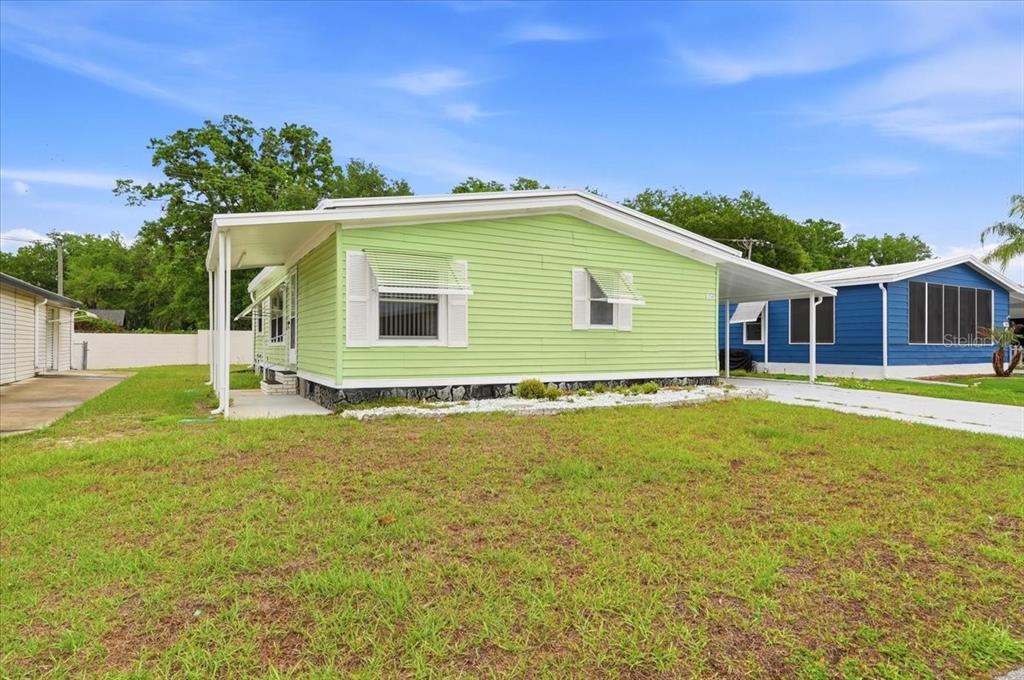 A light green mobile home with white shutters and a carport sits on a grassy lot — 1798 FOX HILL DRIVE, LAKELAND, FL
