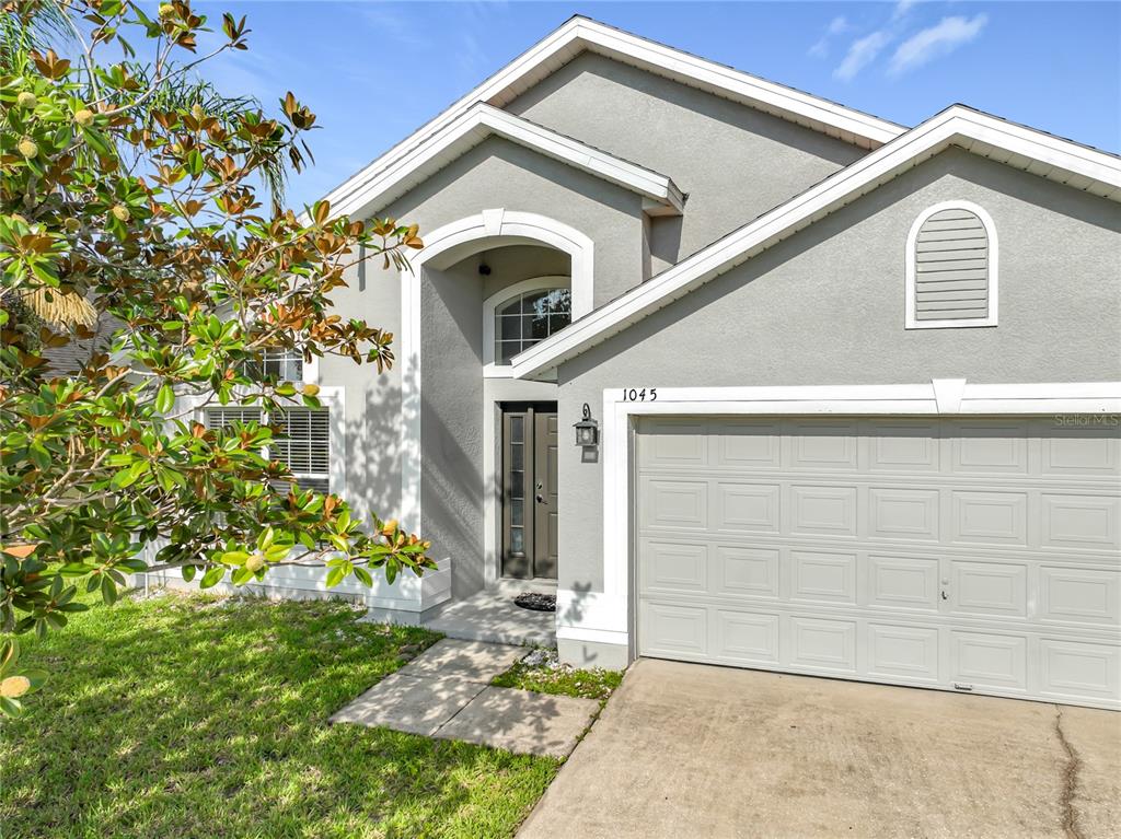 A gray stucco house features a two-car garage, a covered entryway, and a small arched window — 1045 WILLOW BRANCH DRIVE, ORLANDO, FL