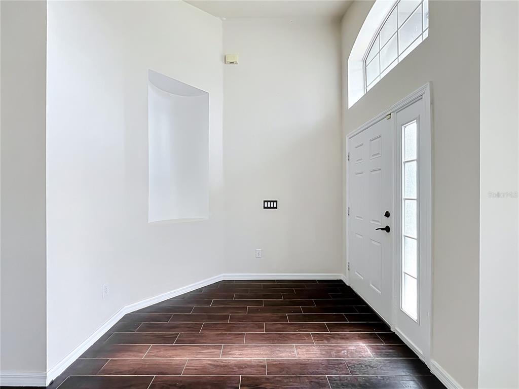 An entryway features dark wood-look tile flooring, high ceilings, and a white front door — 1045 WILLOW BRANCH DRIVE, ORLANDO, FL
