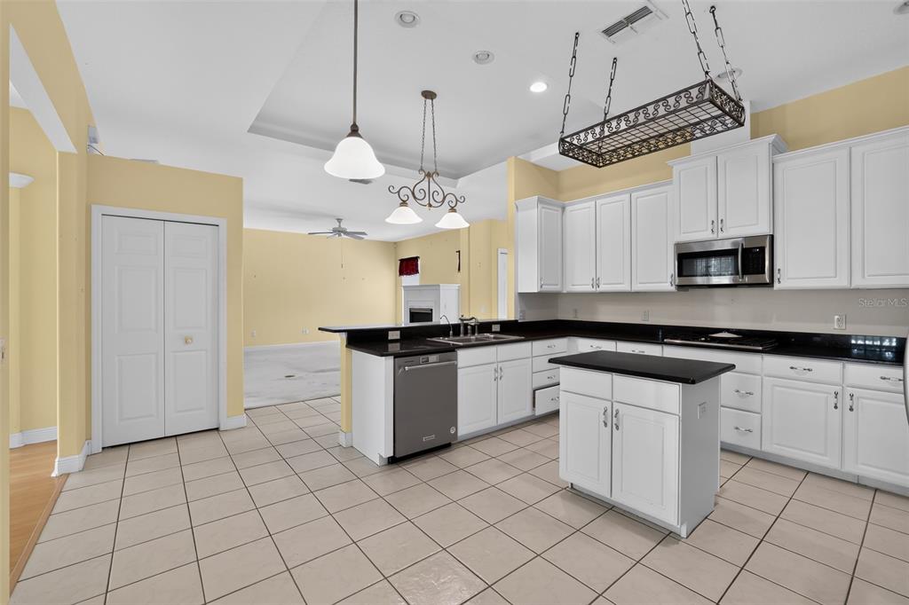 A kitchen with white cabinets, black countertops, a center island, and tiled flooring — 10104 BALCONY STREET, NEW PORT RICHEY, FL