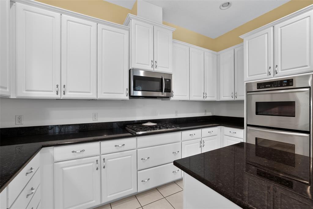 A kitchen with white cabinets, dark granite countertops, a gas cooktop, and stainless steel appliances — 10104 BALCONY STREET, NEW PORT RICHEY, FL