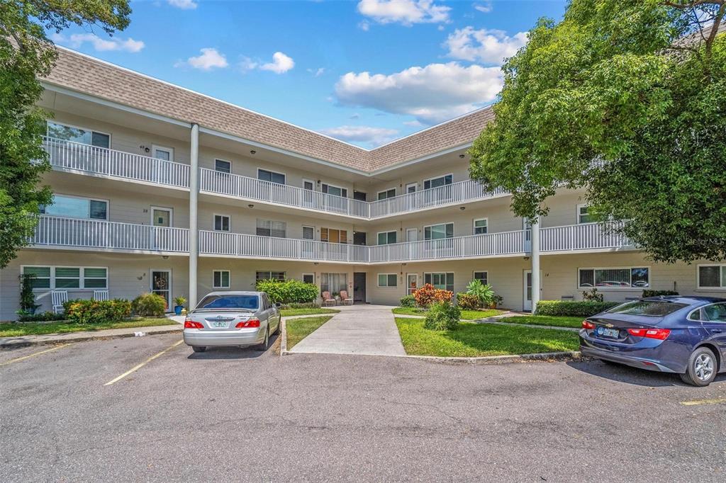 A three-story apartment building with white balconies and a parking lot in the foreground — 2440 WORLD PARKWAY BOULEVARD UNIT 52, CLEARWATER, FL