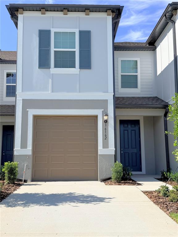 A two-story townhouse exterior features a tan garage door, blue front door, and gray siding — 36162 OBSIDION LANE, ZEPHYRHILLS, FL