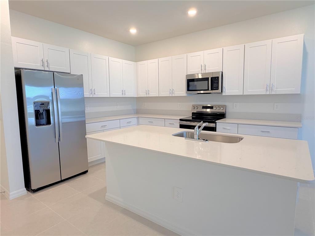 A modern kitchen features white cabinets, stainless steel appliances, and a large quartz-topped island — 36162 OBSIDION LANE, ZEPHYRHILLS, FL