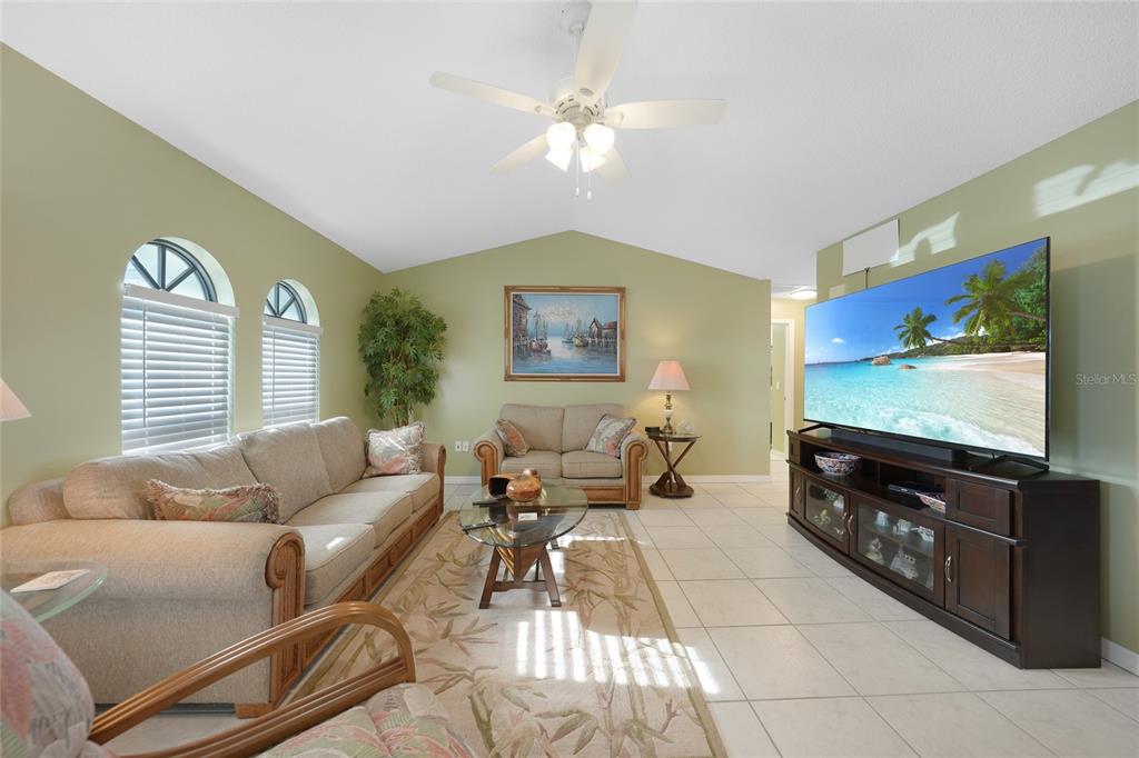 A living room features light green walls, tile flooring, a ceiling fan, and a large television — 3025 CURRY TERRACE, PORT CHARLOTTE, FL