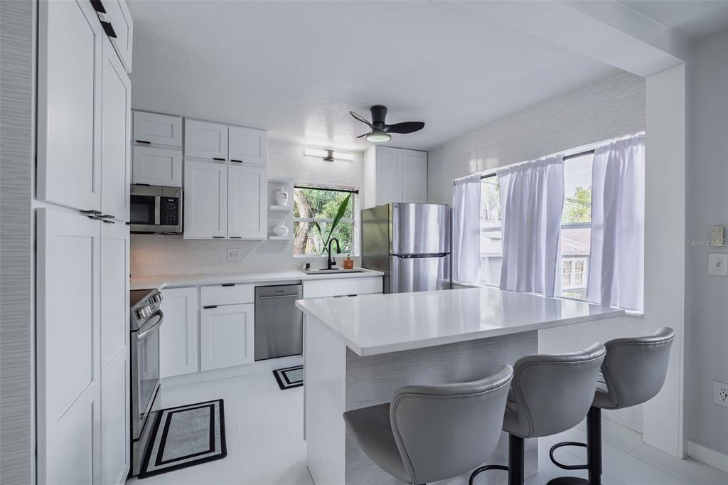 A modern kitchen features white cabinetry, stainless steel appliances, a quartz island, and gray stools — 1427 ASHER LANE, ORLANDO, FL