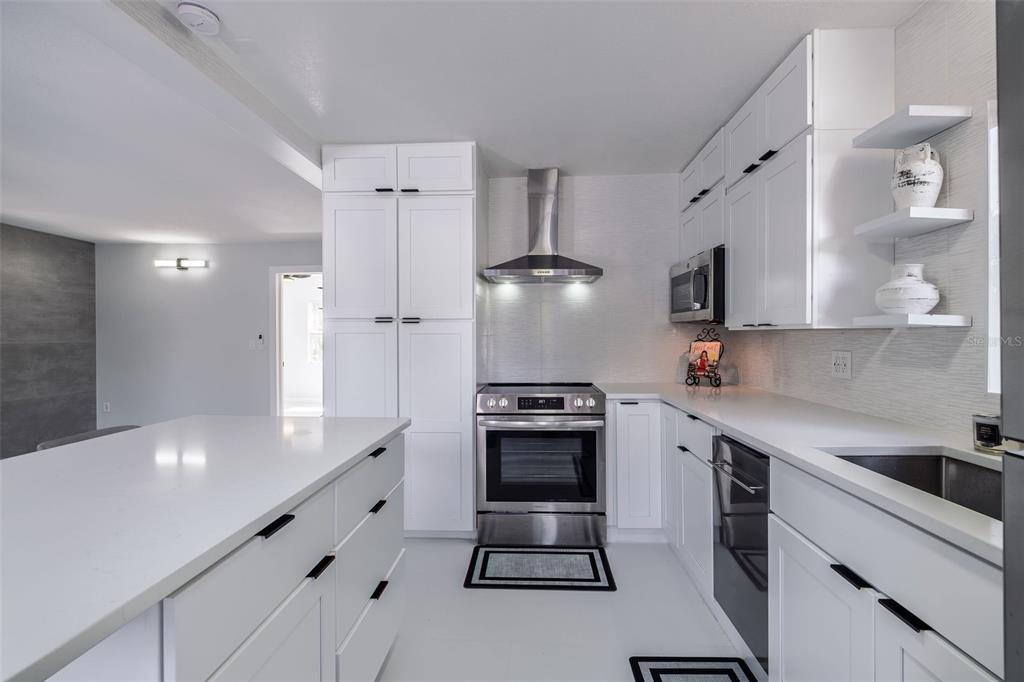 A modern kitchen features white cabinetry, stainless steel appliances, quartz countertops, and an island — 1427 ASHER LANE, ORLANDO, FL