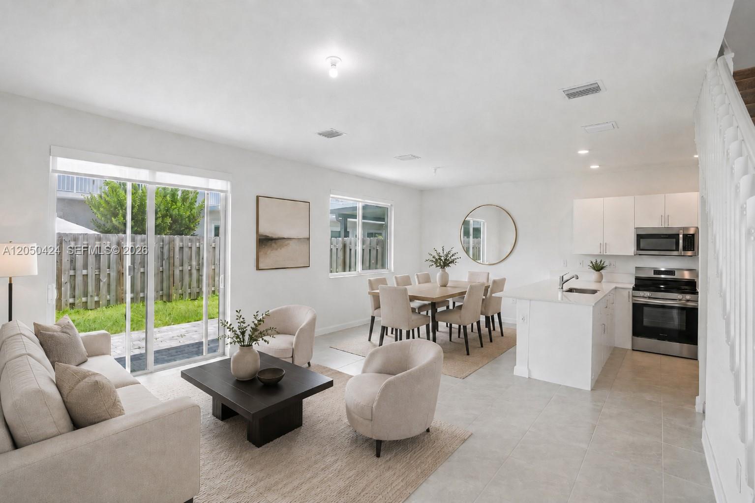An open-concept living and dining area features white cabinets, stainless appliances, and sliding glass doors — 715 SE 15th St, Homestead FL 33034, HOMESTEAD, FL