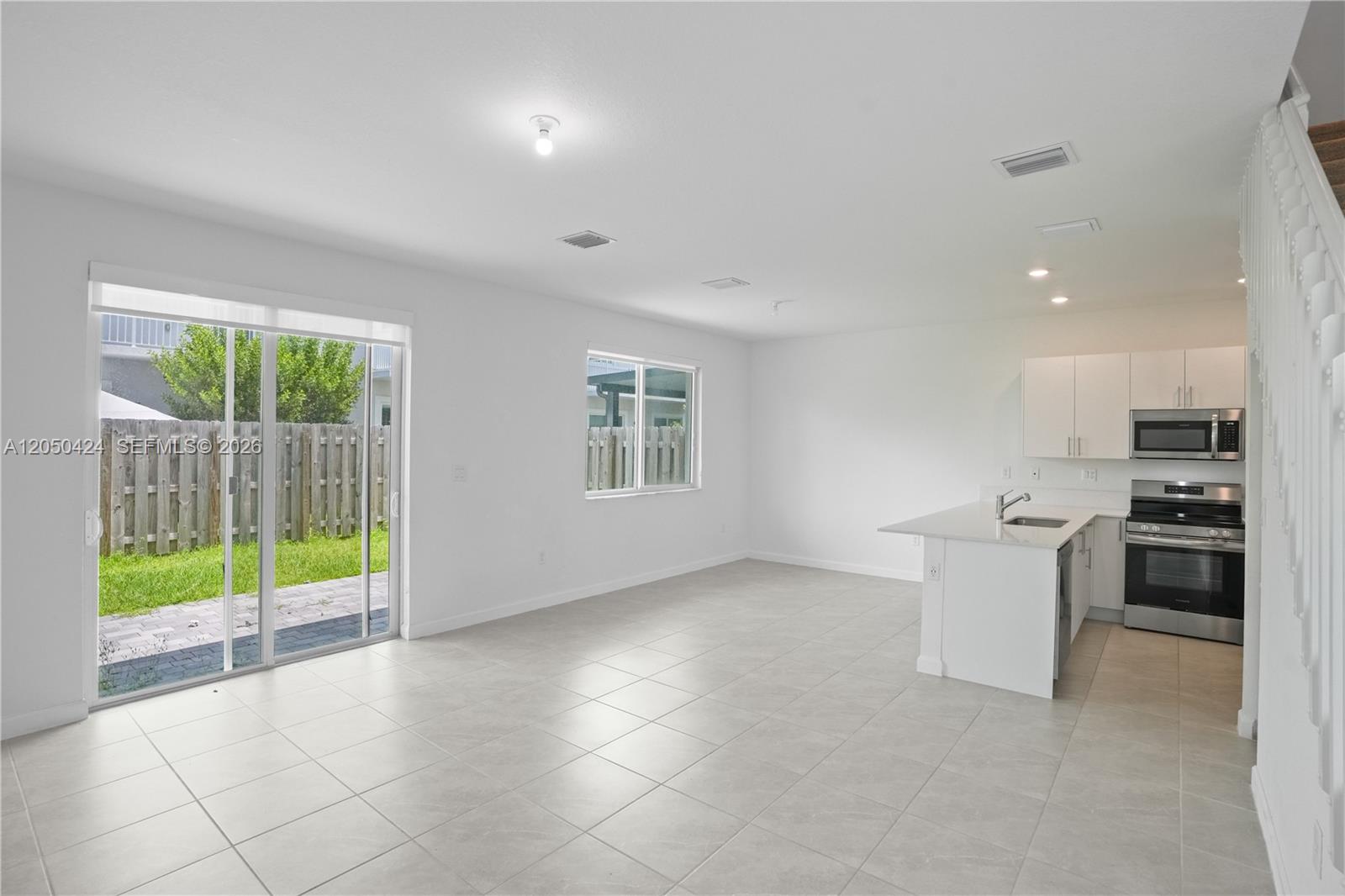 An open-concept kitchen and living area feature white cabinets, stainless appliances, and tile flooring — 715 SE 15th St, Homestead FL 33034, HOMESTEAD, FL