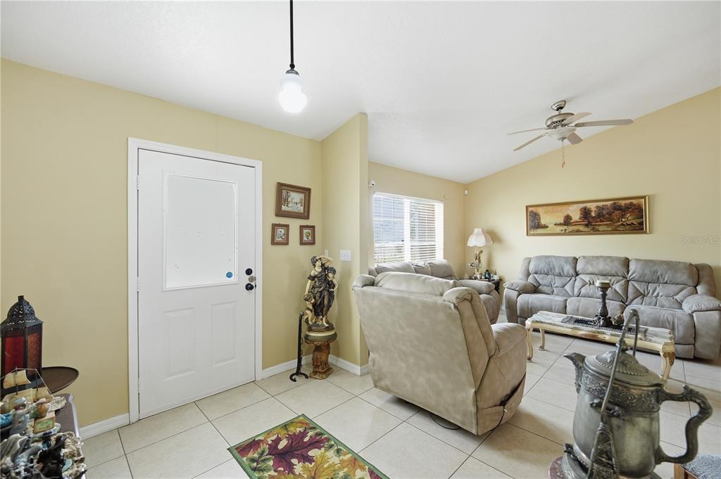 A living room with tile flooring, beige walls, a ceiling fan, and a front door — 642 MADRID DRIVE, KISSIMMEE, FL