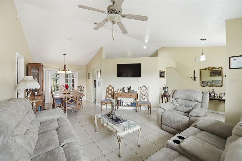 A living room and dining area with vaulted ceilings, tiled floors, and neutral walls — 642 MADRID DRIVE, KISSIMMEE, FL