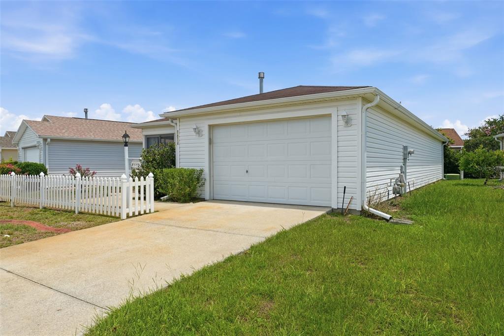 A white, single-story house features a one-car garage, a concrete driveway, and a white fence — 1614 GIBBES WAY, THE VILLAGES, FL