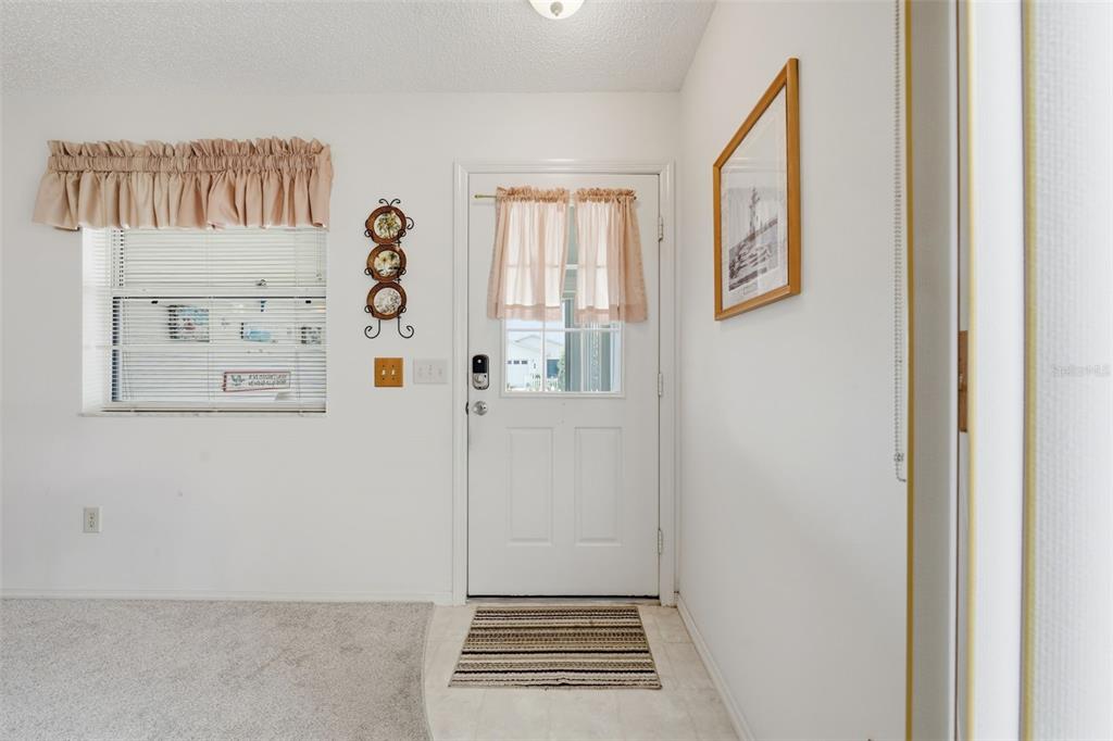 An entryway features a white front door, a window with beige curtains, and carpeted flooring — 1614 GIBBES WAY, THE VILLAGES, FL