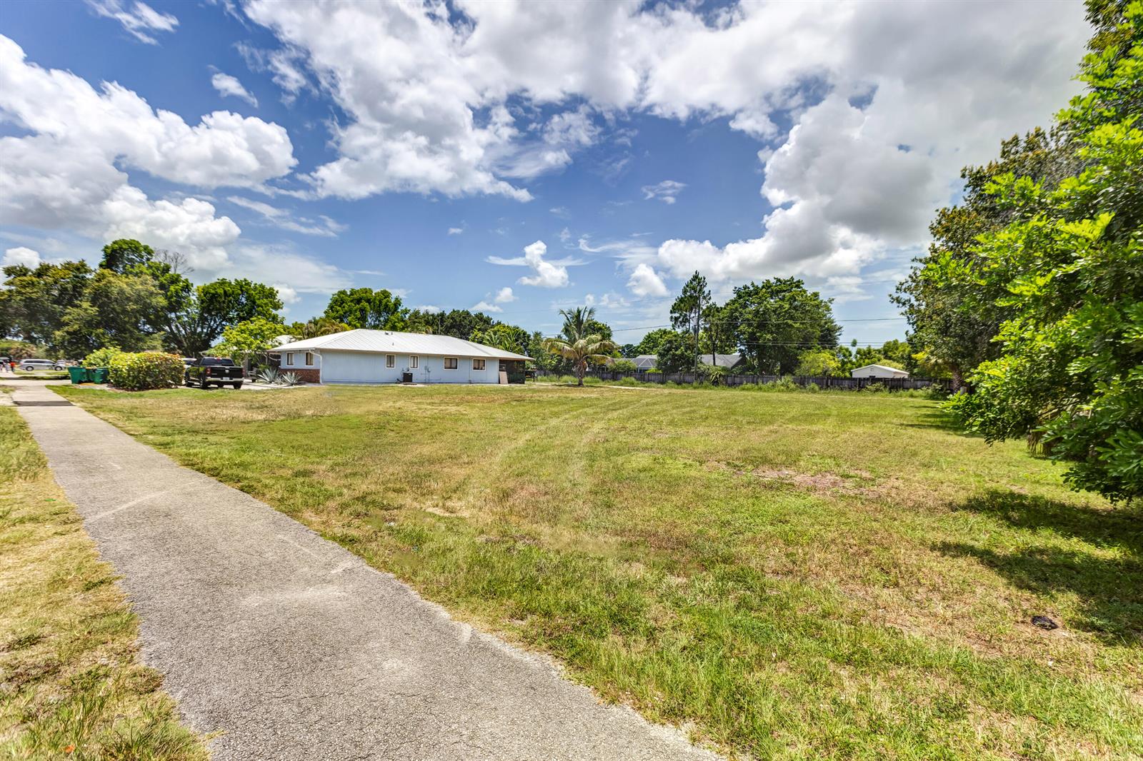 A paved walkway leads toward a white house situated on a large, grassy lot — 2171 Sunshine Boulevard, Naples FL 34116, NAPLES, FL