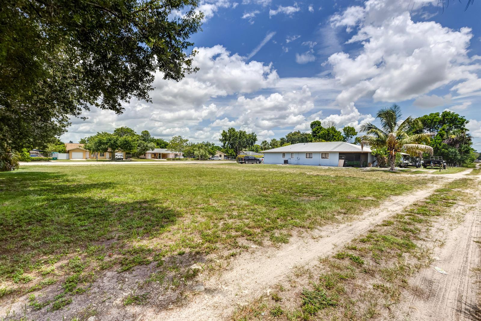 A large, grassy vacant lot sits in front of a light blue house under a cloudy sky — 2171 Sunshine Boulevard, Naples FL 34116, NAPLES, FL