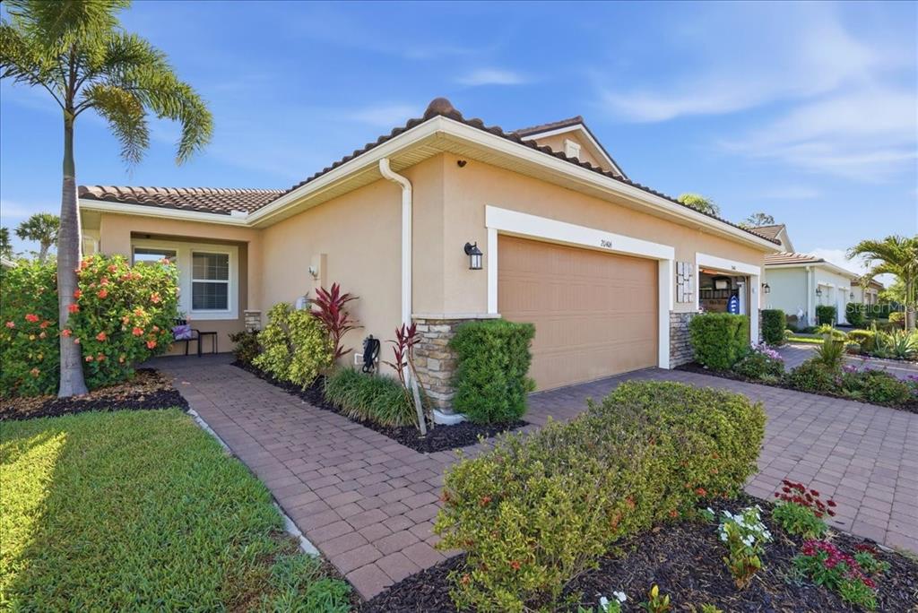 A single-story house with a tan stucco exterior, a two-car garage, and a paved walkway — 20406 GALILEO PLACE, VENICE, FL