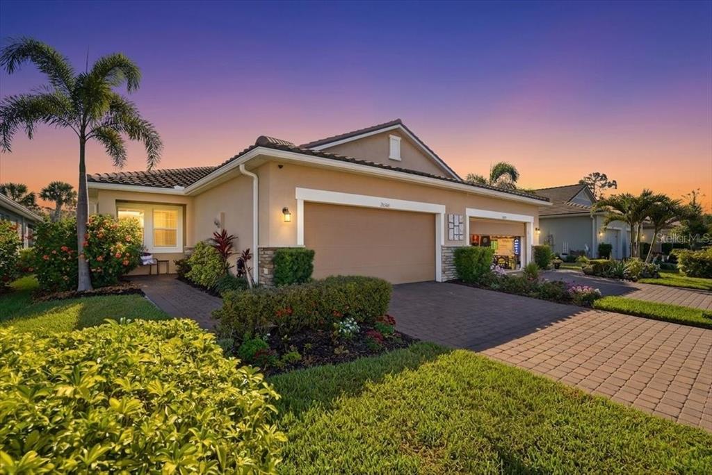 A tan single-story house with a two-car garage and a paved driveway at sunset — 20406 GALILEO PLACE, VENICE, FL