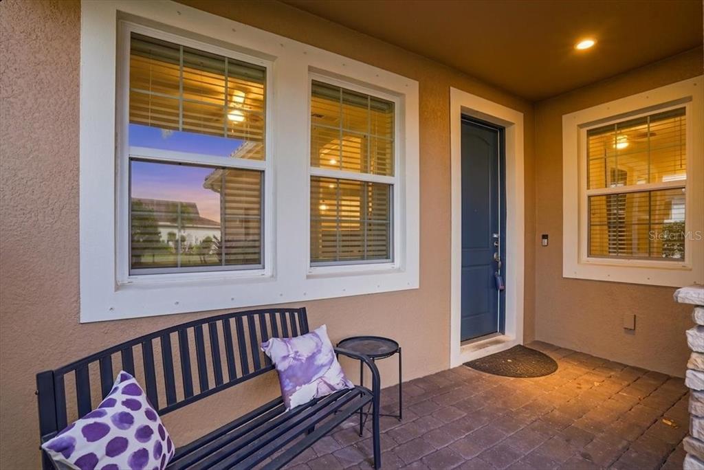 A covered entryway features a dark blue door, a metal bench, and two windows — 20406 GALILEO PLACE, VENICE, FL