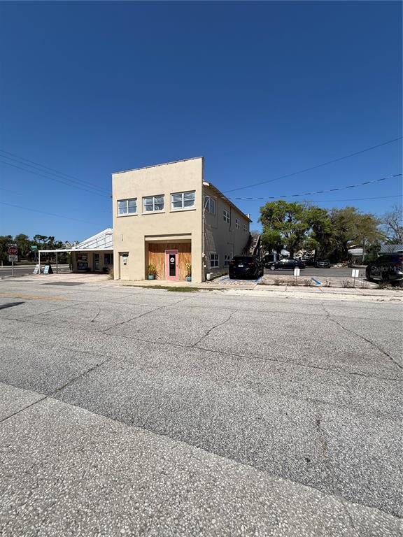 A two-story tan commercial building with a pink front door stands beside a paved road — 225 S DIXIE FREEWAY, NEW SMYRNA BEACH, FL