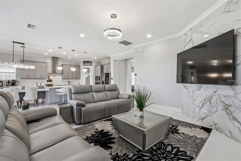 A living room with gray leather sofas, a marble fireplace wall, and an open kitchen — 10863 RUSTIC TIMBER LOOP, SAN ANTONIO, FL
