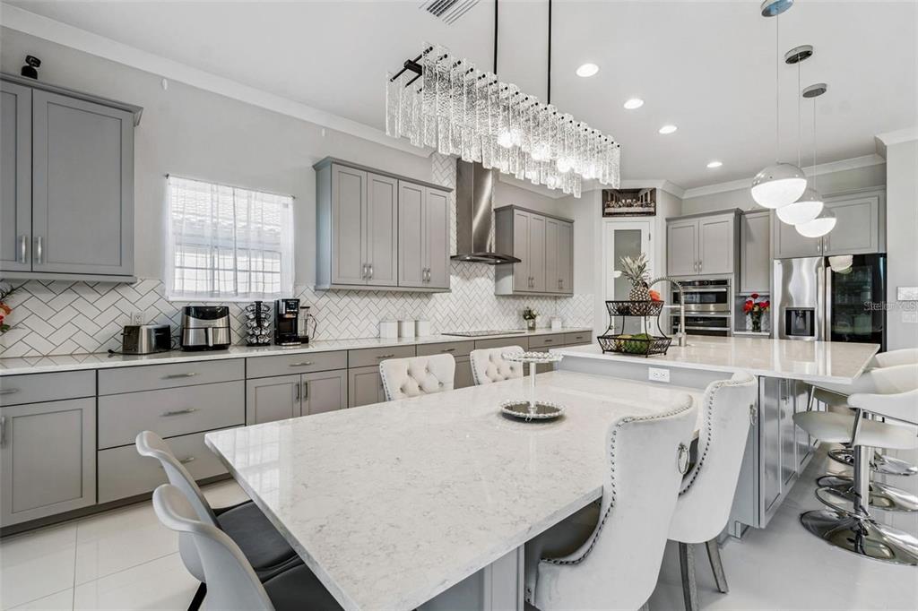 A modern kitchen features gray cabinets, white quartz countertops, a large island, and pendant lighting — 10863 RUSTIC TIMBER LOOP, SAN ANTONIO, FL