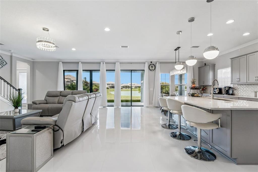 An open-concept living room and kitchen with gray cabinetry, white tile floors, and lake views — 10863 RUSTIC TIMBER LOOP, SAN ANTONIO, FL