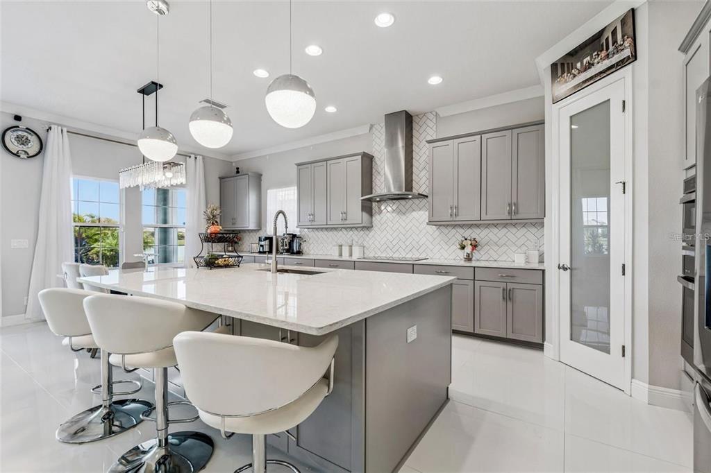 A modern kitchen features gray cabinets, a large white island, and a herringbone tile backsplash — 10863 RUSTIC TIMBER LOOP, SAN ANTONIO, FL