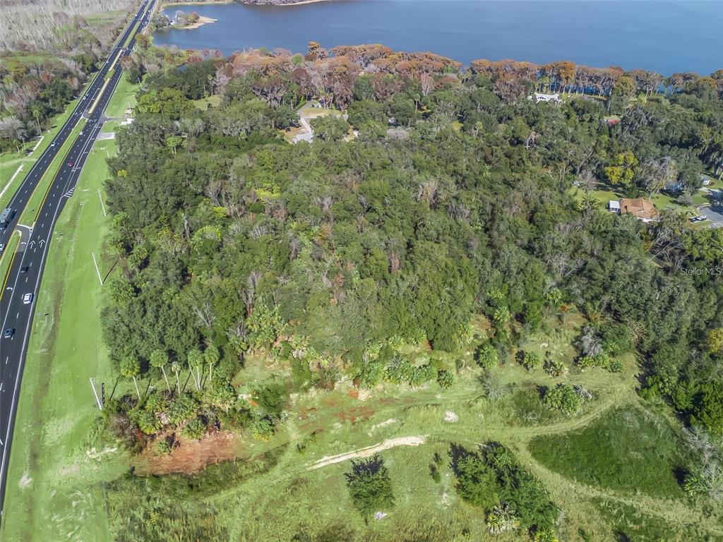 An aerial view shows a large, wooded lot situated between a highway and a lake — S 14TH STREET, LEESBURG, FL