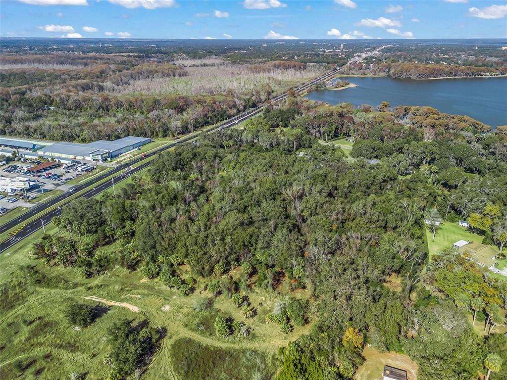 An aerial view shows a large, wooded lot adjacent to a highway and a lake — S 14TH STREET, LEESBURG, FL