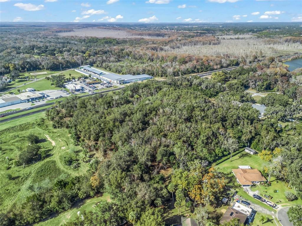 An aerial view shows a large wooded lot adjacent to a commercial building and road — S 14TH STREET, LEESBURG, FL