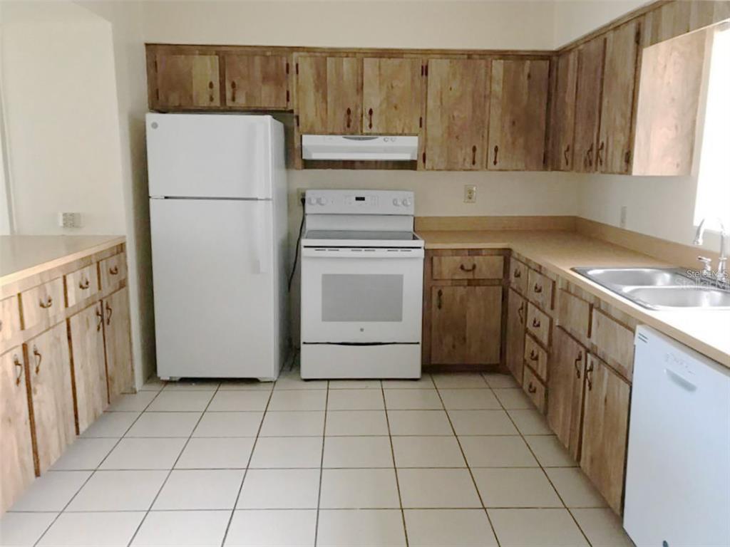 A kitchen features wood cabinets, white appliances, a tiled floor, and laminate countertops — 1106 N HOAGLAND BOULEVARD, KISSIMMEE, FL