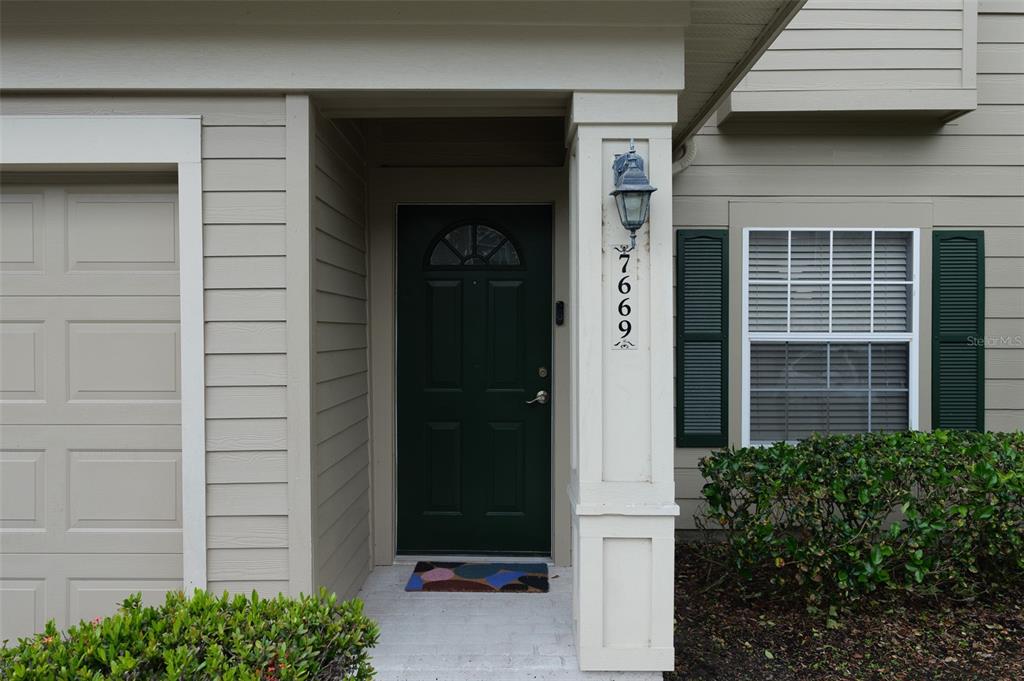 The exterior view shows a beige house entrance with a dark green door and shutters — 7669 PLANTATION CIRCLE UNIT 7669, BRADENTON, FL