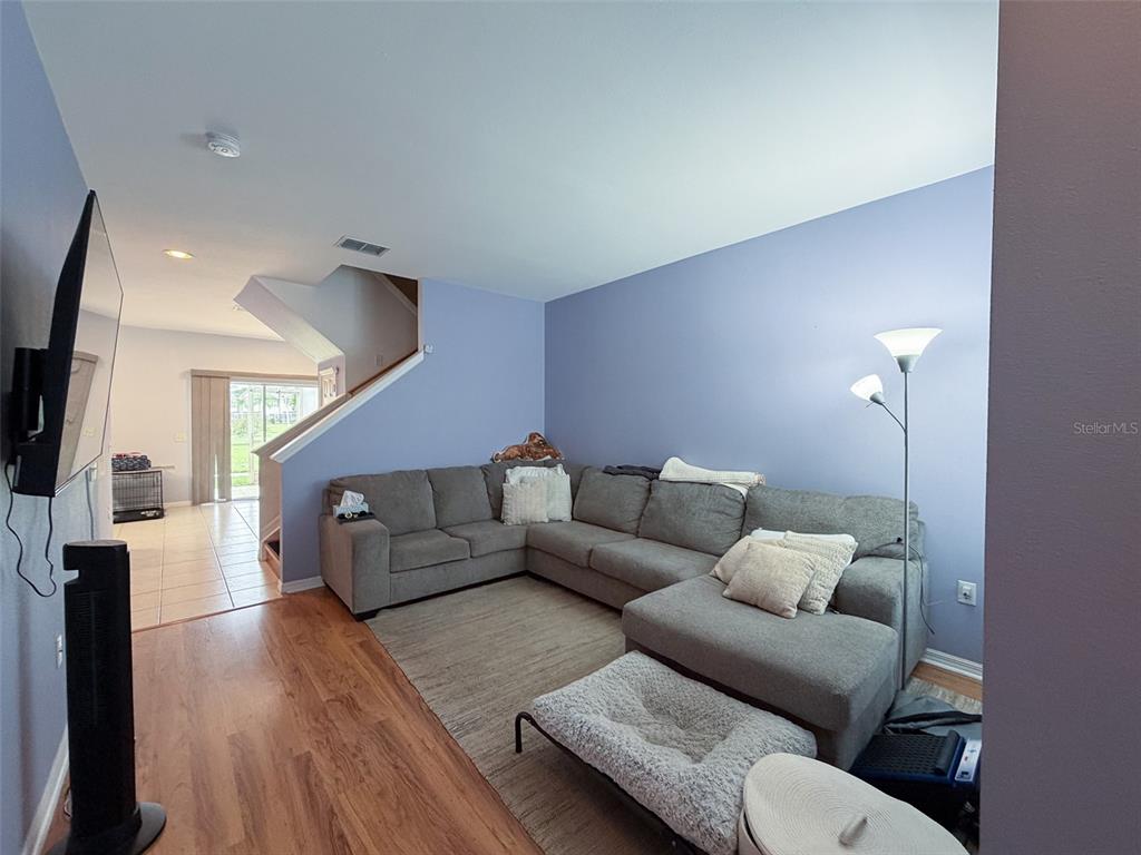 A living room with wood flooring, blue walls, and a staircase leading to an upper level — 7669 PLANTATION CIRCLE UNIT 7669, BRADENTON, FL