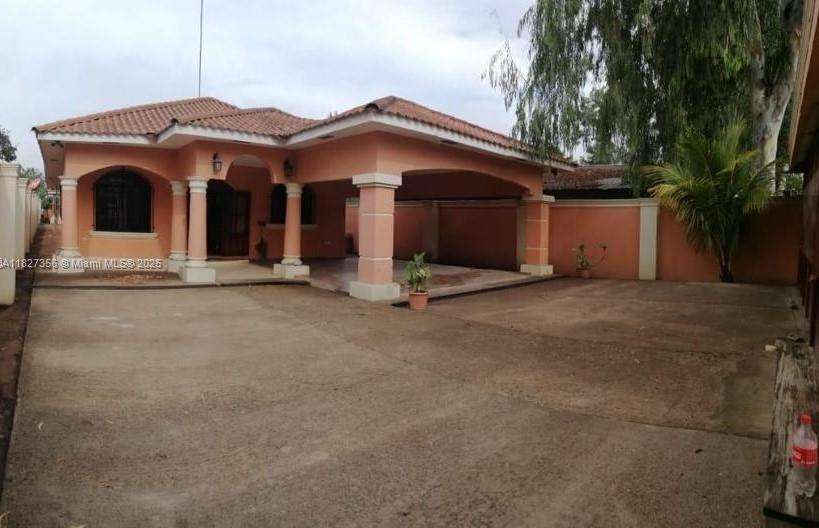 A single-story peach-colored house with a large concrete driveway and a covered carport — 0000 Calle Principal Guinope, FL, FL