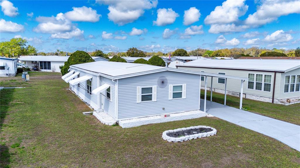 A light gray manufactured home features a front carport, white shutters, and a stone planter — 5541 BENTON STREET, ZEPHYRHILLS, FL
