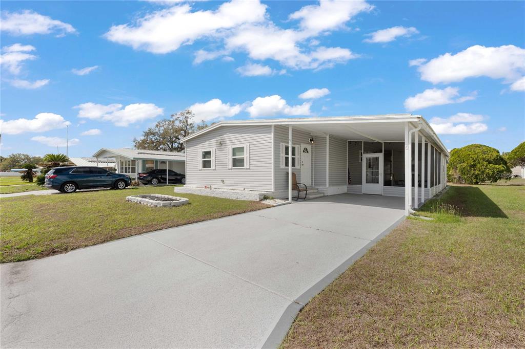 A light blue mobile home with a white roof and a carport sits on grass — 5541 BENTON STREET, ZEPHYRHILLS, FL