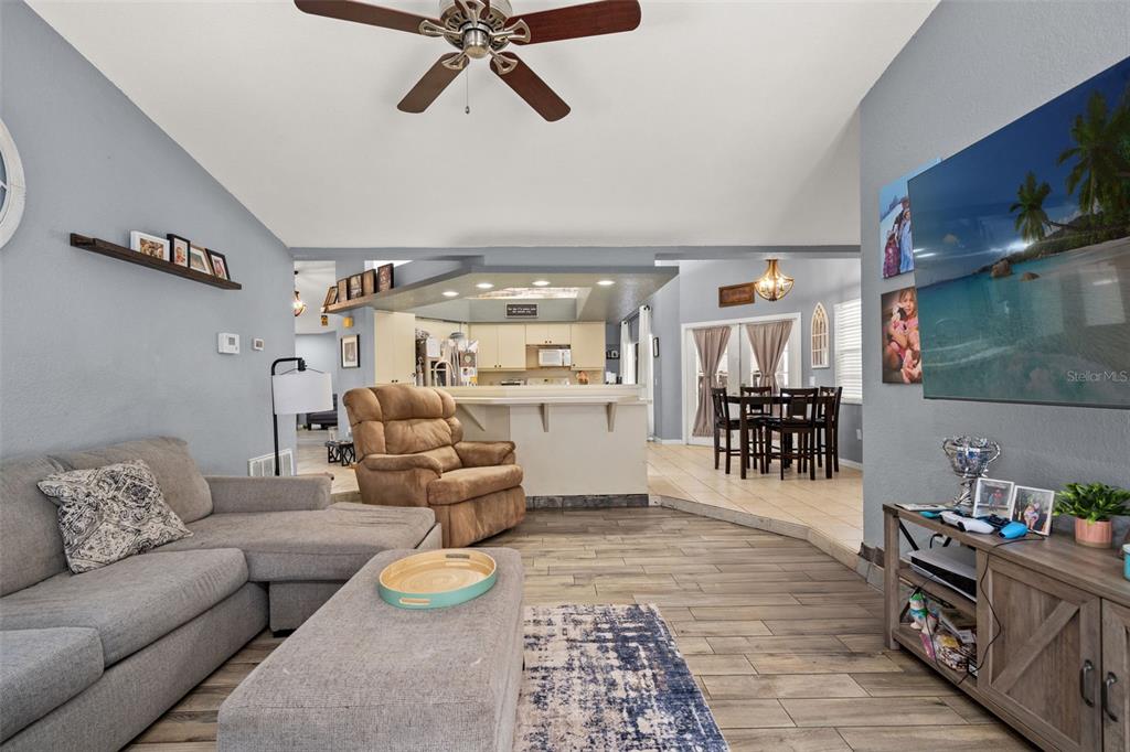 A living room with gray walls, wood-look tile flooring, a sectional sofa, and a television — 13499 BRUNI DRIVE, SPRING HILL, FL