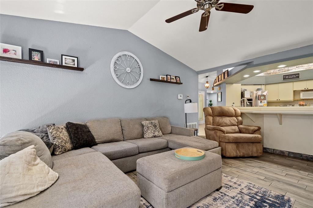 A living room features a grey sectional sofa, a brown recliner, and a large wall clock — 13499 BRUNI DRIVE, SPRING HILL, FL