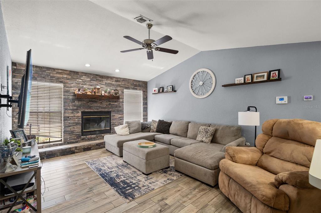 A living room features a stone fireplace, a gray sectional sofa, and a brown recliner — 13499 BRUNI DRIVE, SPRING HILL, FL
