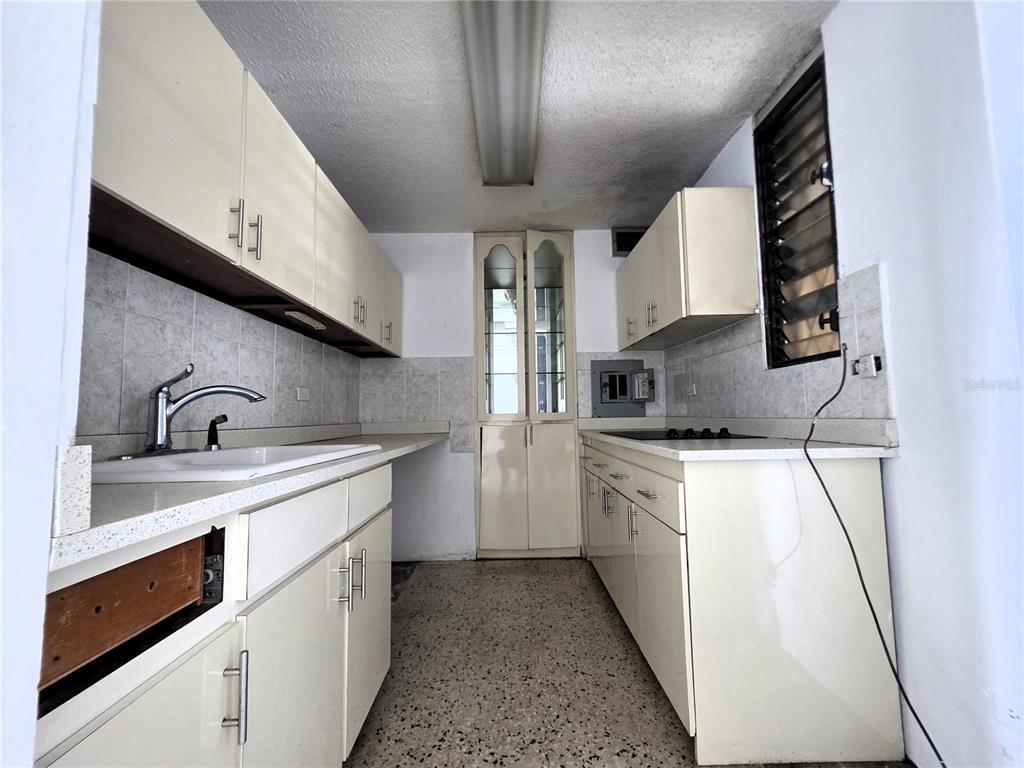 A galley-style kitchen features cream-colored cabinets, a white countertop, and a speckled tile floor — 65 CALLE SANTIAGO IGLESIAS UNIT 802, SAN JUAN, PR