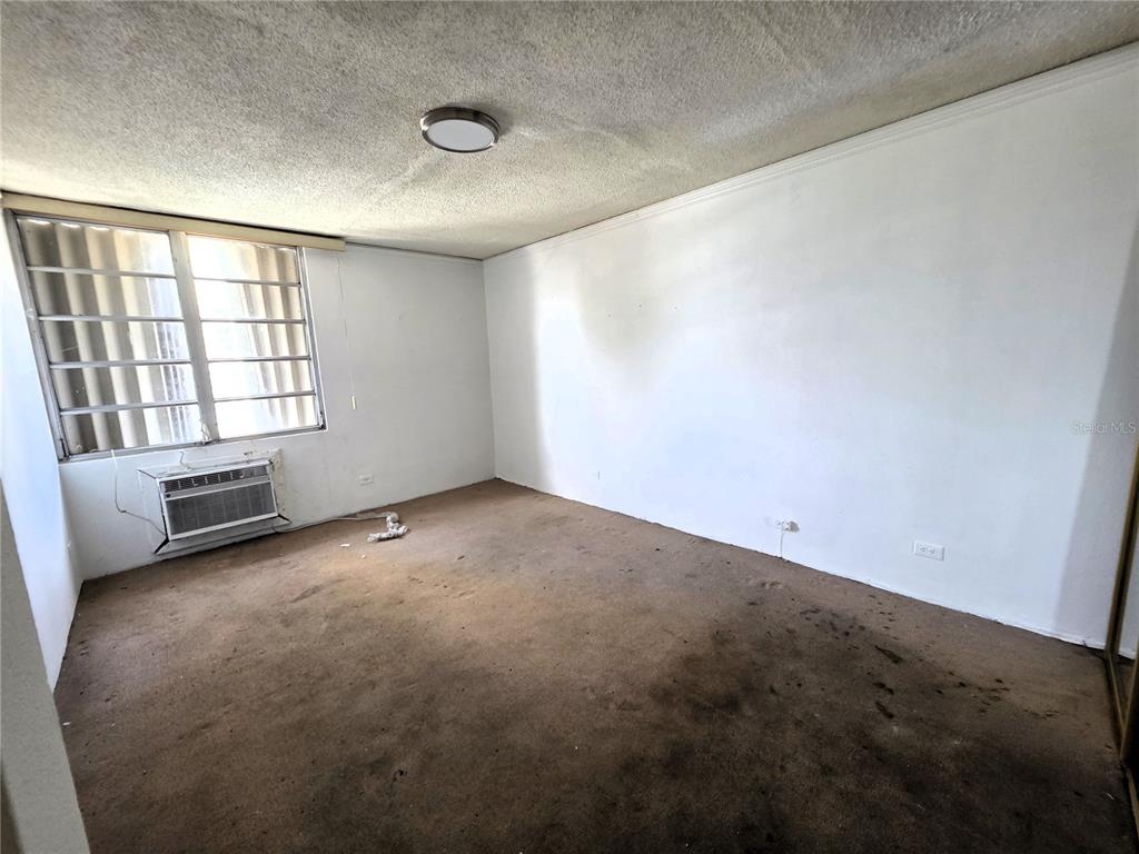 An empty bedroom features a window with security bars, a wall-mounted air conditioner, and carpet — 65 CALLE SANTIAGO IGLESIAS UNIT 802, SAN JUAN, PR