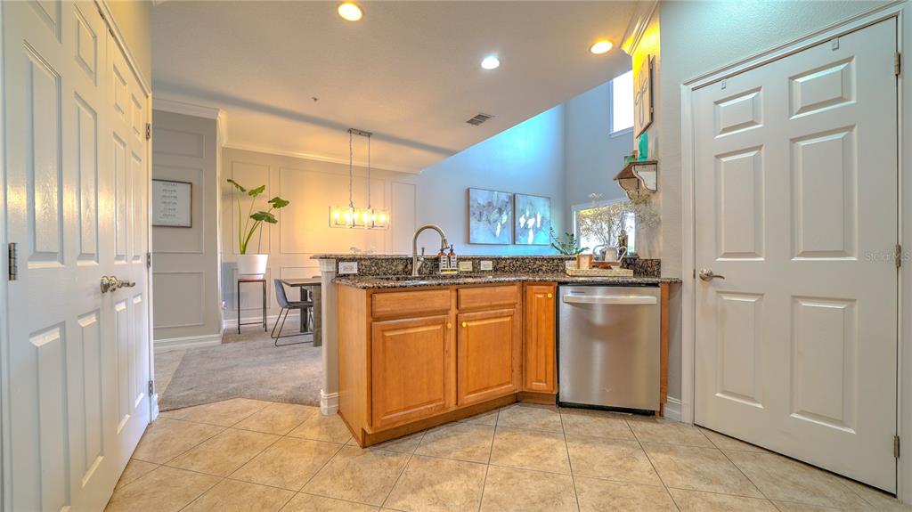 A kitchen with wood cabinets, granite countertops, and stainless steel appliances opens to a dining area — 10455 BELFRY CIRCLE, ORLANDO, FL
