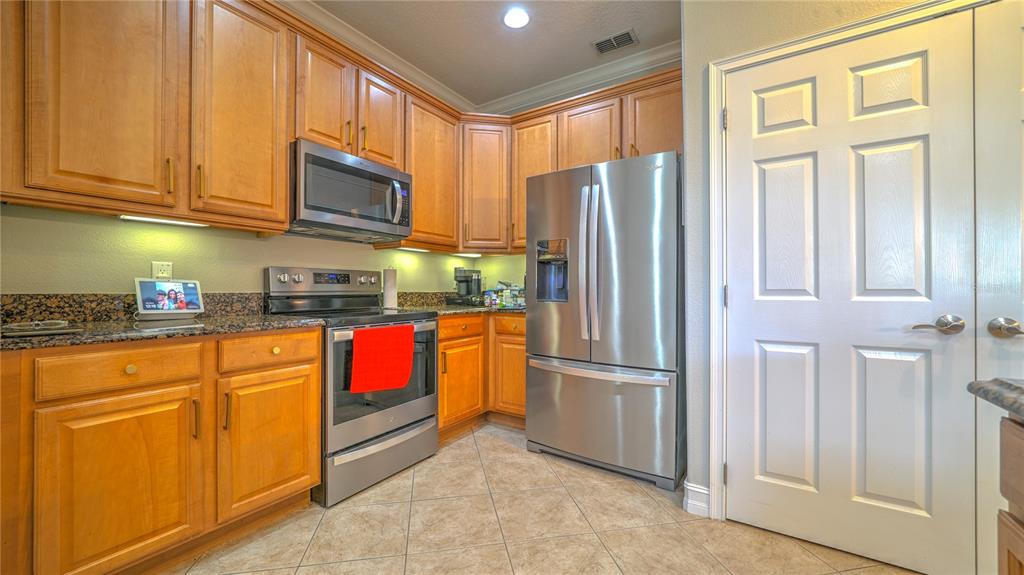 A kitchen features wood cabinets, stainless steel appliances, granite countertops, and tile flooring — 10455 BELFRY CIRCLE, ORLANDO, FL